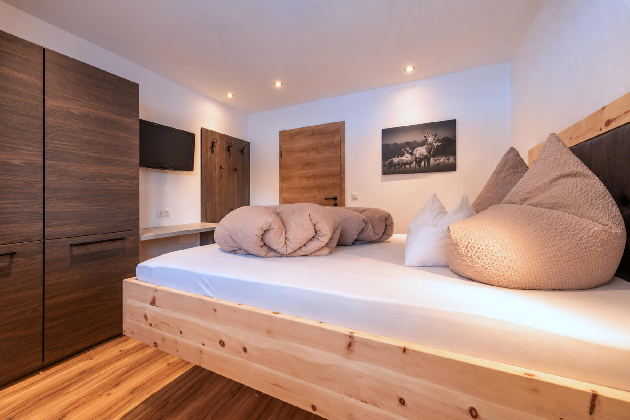 Schlafzimmer im Appartement Finn mit handgefertigtem Zirbenholzbett, gemütlichen Kissen, Holzschrank und Fernseher.